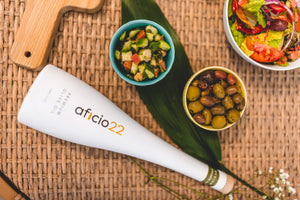 a white bottle of aficio22 olive oil laying on a table top next to an array of small plates of olives and salads