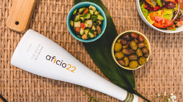 a white bottle of aficio22 olive oil laying on a table top next to an array of small plates of olives and salads